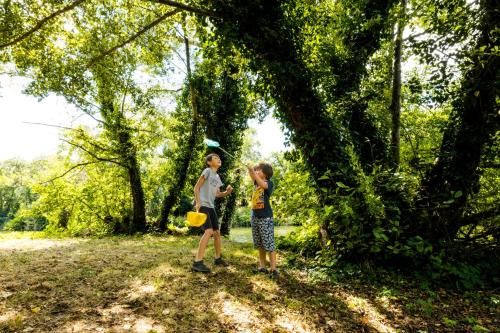 two children standing under a tree in a field at Camping Onlycamp le Clos Imbert in Thouars