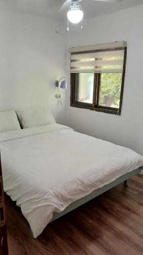 a white bed in a room with a window at Little Hula in Yesod Hamaala