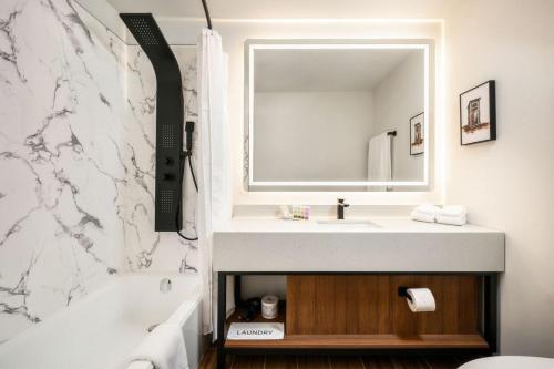 a bathroom with a sink and a mirror and a tub at Acclaim Hotel by CLIQUE in Calgary