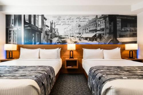two beds in a hotel room with a painting on the wall at Acclaim Hotel by CLIQUE in Calgary