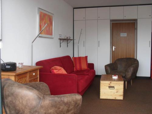 a living room with a red couch and two chairs at Nordnordwest in Langeoog