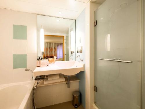 a bathroom with a sink and a tub and a mirror at Novotel Birmingham Centre in Birmingham