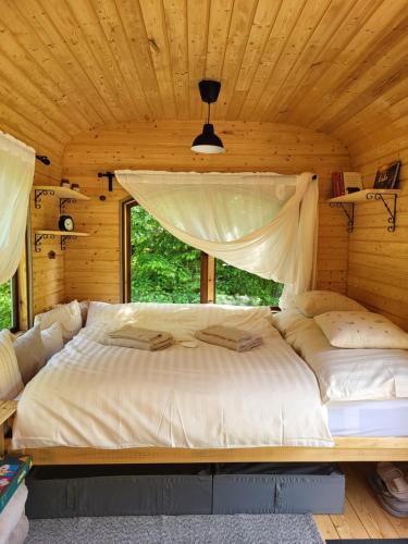 a large bed in a wooden room with a window at Glamping Maringotka77 in Protivec