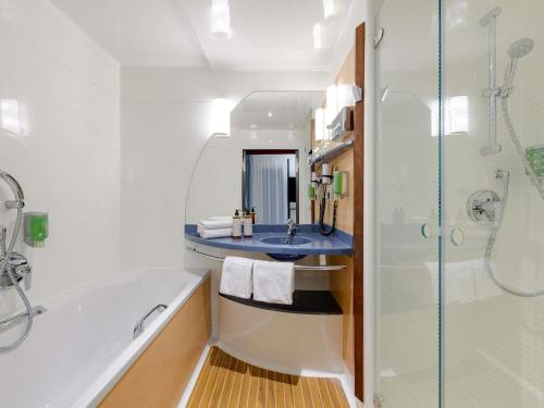 a bathroom with a tub and a sink and a shower at Novotel Suites München Parkstadt Schwabing in Munich