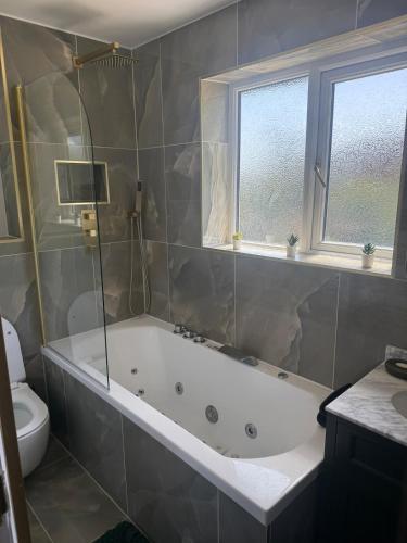 a bathroom with a tub and a toilet and windows at The Hideaway Aylesbury in Buckinghamshire