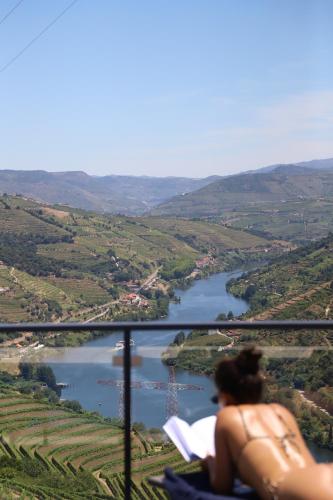 a woman sitting on a chair reading a book next to a river at Casa Vale do Douro in Mesão Frio