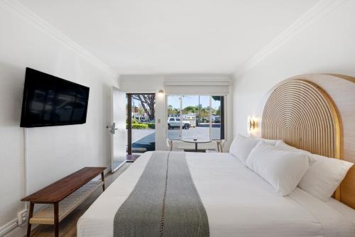 a white bedroom with a large bed and a tv at Sunset Motel in Santa Barbara