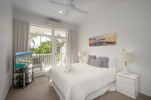 a white bedroom with a bed and a tv at Sandy Beach Resort in Noosaville