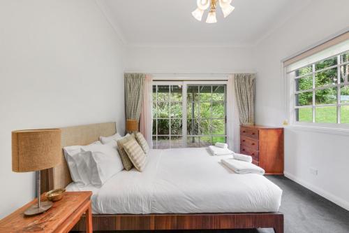 a bedroom with a bed and a table and windows at Alcheringa Cottage Amazing Location with views in Kangaroo Valley