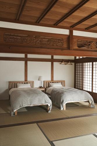 two beds in a room with wooden ceilings and windows at TOKIWA葛城-katsuragi- in Shinjō