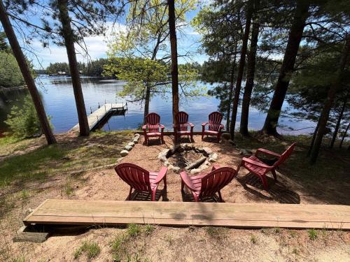 a group of chairs sitting around a fire pit by the water at Little Red Lakeside Cabin in Three Lakes