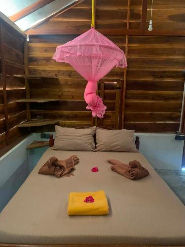 a bed with a pink umbrella and towels on it at Thambili cabanas whisky point in Arugam Bay