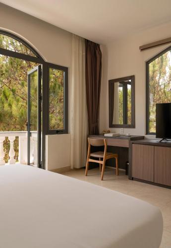 a bedroom with a bed and a desk and windows at Rung La Kim Resort in Da Lat