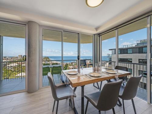 a dining room with a table and chairs and windows at Aurora Pacific Unit 12 in Caloundra