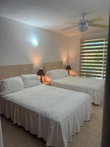 two beds in a bedroom with white sheets and a fan at Los Mangos in Zihuatanejo