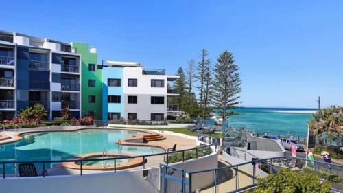 a swimming pool next to a building with the ocean at Grand Pacific Unit 10 in Caloundra