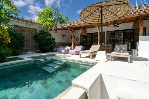 a pool with chairs and an umbrella next to a house at Villa Ruta II - Luxury 2BR Tropical Villa next to Luna Beach Club and Nyanyi beach in Tanah Lot