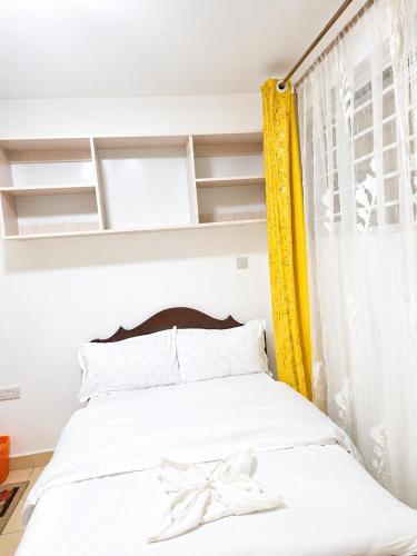 a bedroom with a white bed with a yellow curtain at Phonex haven near Westside Mall in Nakuru
