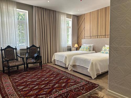 a bedroom with two beds and a chair and two windows at Hotel Jipek Joli in Nukus