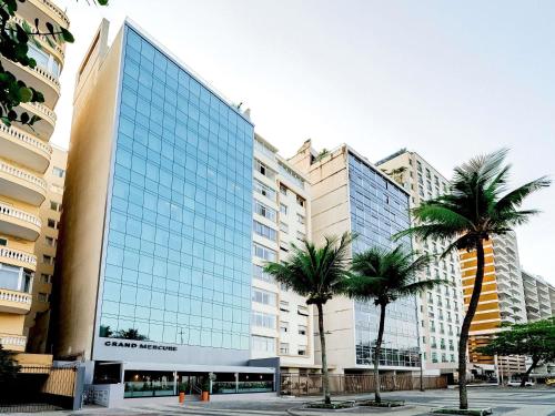 a large glass building with palm trees in front of it at Grand Mercure Rio de Janeiro Copacabana in Rio de Janeiro