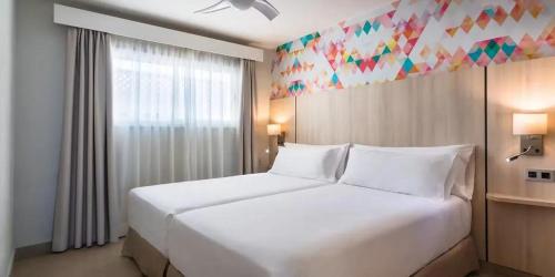 a bedroom with a large white bed and a window at Servatur Isora Suites in Puerto de Santiago