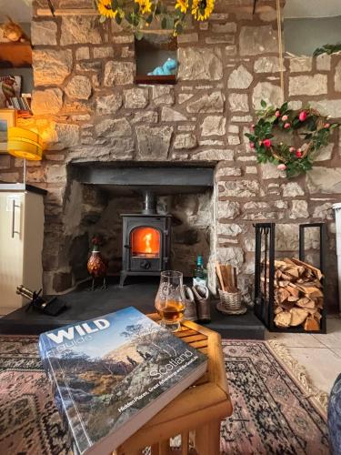 a living room with a stone fireplace with a book on a table at Loch Ness village cottage for 2 with free parking & pets welcome in Drumnadrochit