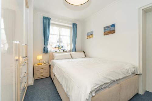 a bedroom with a white bed and blue curtains at Syltglück in Westerland