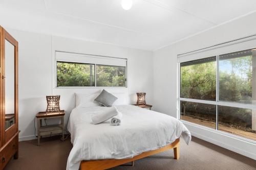 a white bedroom with a bed and two windows at Fennell House in Robe