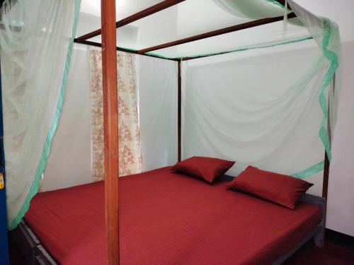 a canopy bed with two red pillows in a room at Eastwind Surf Camp - Surf & Stay in Arugam Bay