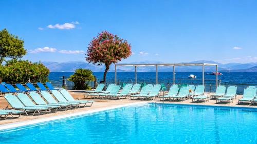 a pool with chairs and the ocean in the background at Agnes Beach Hotel Apartments in Kavos