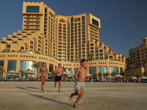 three men running on the beach in front of a hotel at Fairmont Ajman in Ajman 
