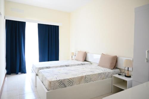 a white bedroom with a bed with blue curtains at Hotel Rocha in Ribeira Grande
