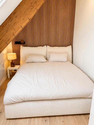 a white bed in a room with a wooden ceiling at Wonenmeteenknipoog Groningerweg 23D in Peize