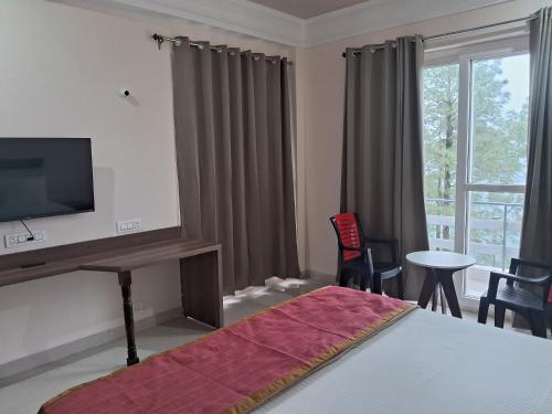 a bedroom with a bed with a television and a table and chairs at Shivansh Hotel in Kānda