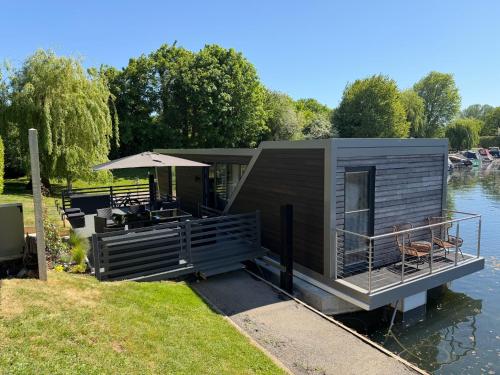 a tiny house on the water with an umbrella at Escape to Willow Wharf - A Luxury Thames Houseboat in Chertsey