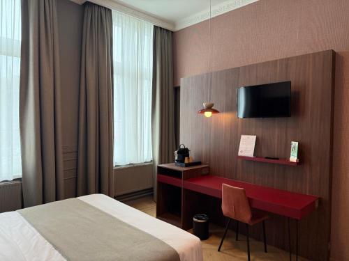 a hotel room with a bed and a desk with a tv at Hotel Amfora in Poperinge