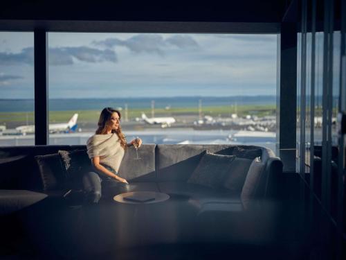 a woman sitting on a couch at an airport at Pullman Auckland Airport in Auckland