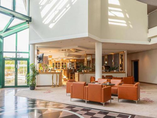 オーバーディングにあるAtomis Hotel Munich Airport by Mercureのオレンジ色の椅子とテーブルが置かれたホテルのロビー