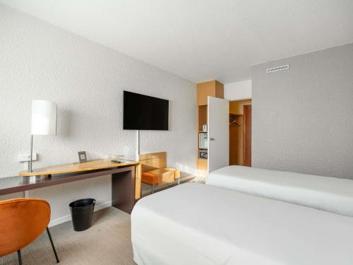 a hotel room with two beds and a desk at Novotel Poissy Orgeval in Orgeval