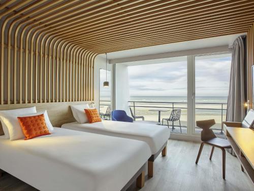two beds in a room with a view of the ocean at Novotel Thalassa Le Touquet in Le Touquet-Paris-Plage