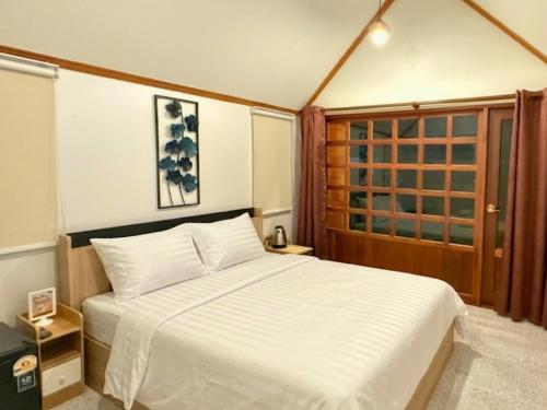a bedroom with a white bed and a wooden door at สวนไมตรีจิต รีสอร์ท Suan Maitrichit Resort in Ban Khlong Si