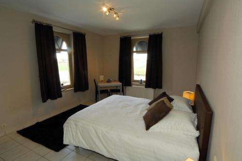 a bedroom with a white bed and two windows at Hôtel Le Saint Loup in Gembloux