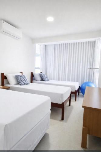 a hotel room with three beds and a table at Apartamento Confortável na Praia do Morro in Guarapari