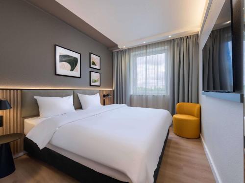 a hotel room with a large white bed and a yellow chair at ibis Paderborn City in Paderborn