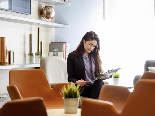 a woman sitting on a table reading a magazine at Novotel Frankfurt City in Frankfurt