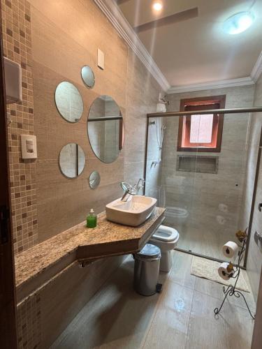a bathroom with a sink and a toilet and mirrors at Dara House apart e eventos com piscina, sauna, Jacuzzi e área gourmet para festas in Cachoeira do Campo