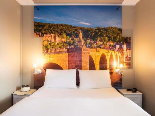 a bedroom with a large bed with a painting of a bridge at ibis Heidelberg Hauptbahnhof in Heidelberg