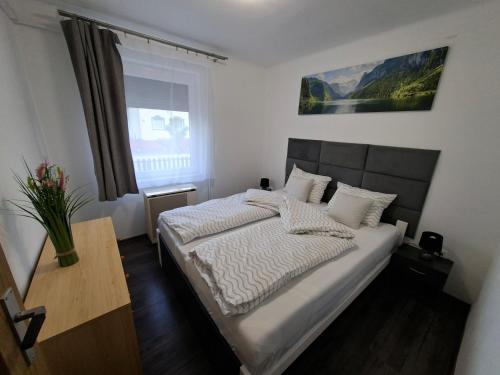 a bedroom with a bed with white sheets and a window at Kakukkfészek Apartmanok in Kiskunmajsa