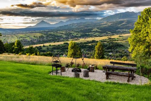a picnic table and bench in a field with mountains at Domki Widokowe Wooden Pod Gubałówką z Jacuzzi in Ząb