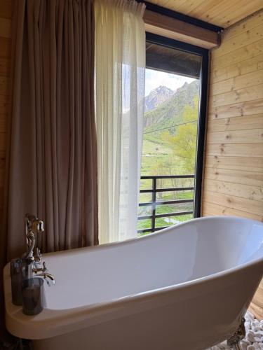 a bath tub in a bathroom with a large window at Tera Cottages kazbegi in Kazbegi